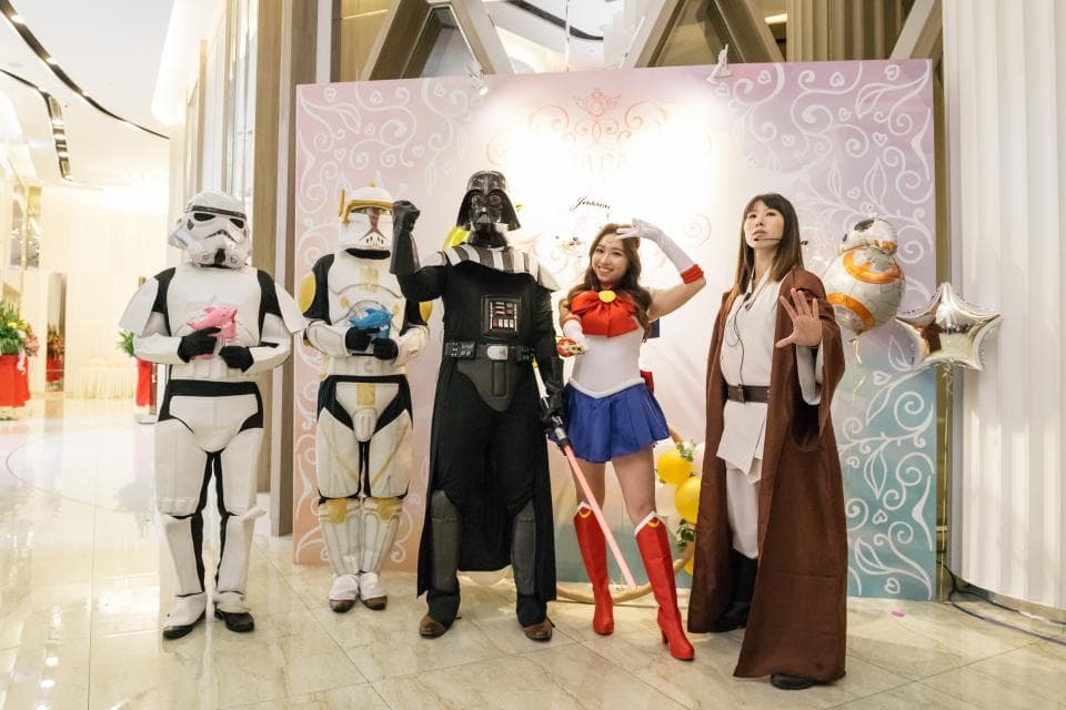 這張照片是一個以星球大戰為主題的派對,照片中最重要的一部分是派對的主角們:穿著星球大戰角色服裝的參加者們。他們站在佈置精美的背景板前,擺出各種姿勢,看起來非常開心。