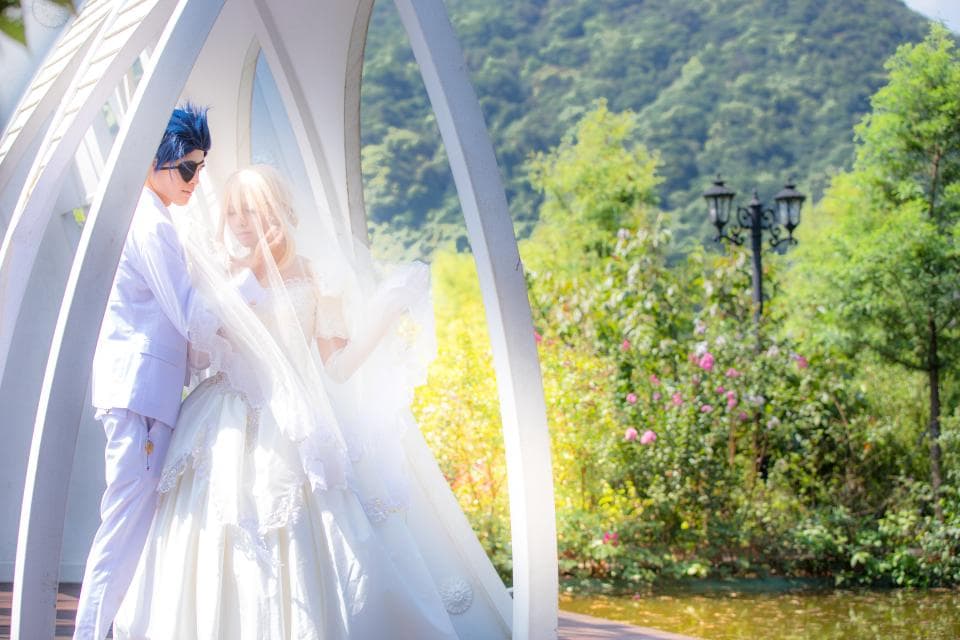 這張照片是一對新人站在一個白色的拱門下,新娘穿著白色婚紗,新郎穿著白色西裝,他們面帶微笑,看起來非常幸福。