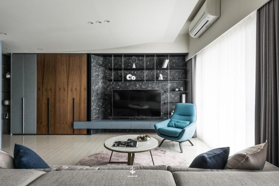 這張客廳的照片是一個現代化的空間,有大型的電視牆,上面有黑色的石材和層架,以及一個藍色的單人沙發,旁邊有一個咖啡桌。