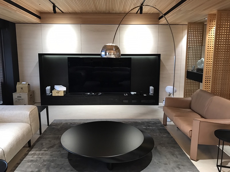 這張照片是一間現代化的客廳,有一個大型的黑色電視牆,上面裝著一臺大電視,牆壁上還有一盞弧形落地燈,燈光柔和。客廳中央擺著一張黑色圓形茶几,兩旁分別有一張沙發和一張單人座。