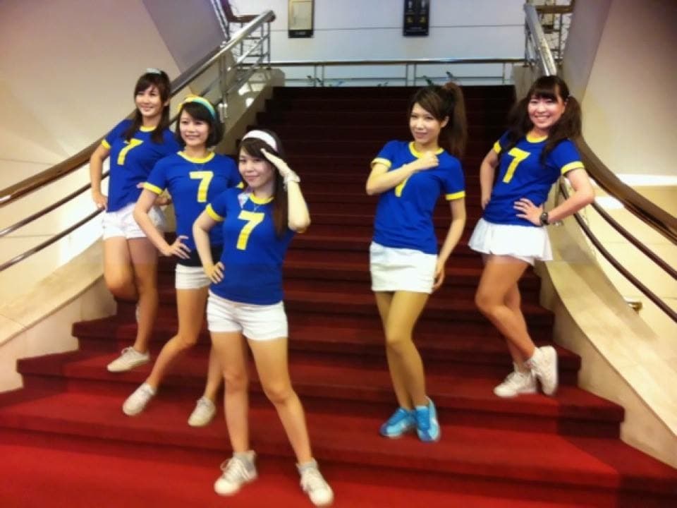 這張照片是四個穿著藍色運動服的女孩站在紅色的樓梯上,其中一個女孩穿著藍色的制服,上面印著數字「7」。她們似乎在為一場比賽或活動加油。