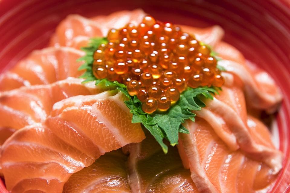 這張「鮭魚卵蓋飯」的照片是一碗日式蓋飯,上面放滿了新鮮的鮭魚片和橘色的鮭魚卵,看起來非常美味。