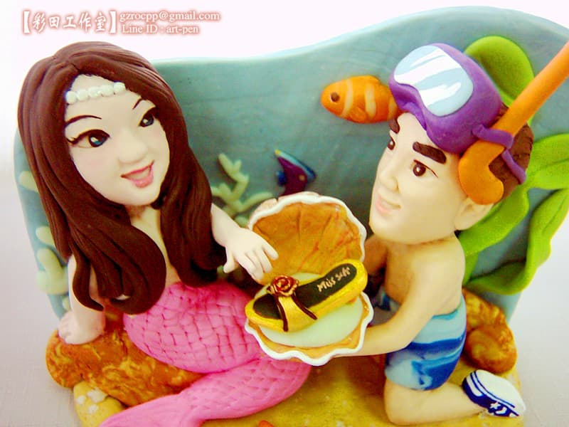 這張照片是一對可愛的卡通人物,一個是美人魚,另一個是潛水員,他們似乎正在一個浪漫的海底世界中相遇。美人魚穿著粉紅色的魚尾,而潛水員則戴著潛水鏡和氧氣筒,他們的表情都顯得十分幸福,背景是一片清澈的海水和美麗的珊瑚礁。