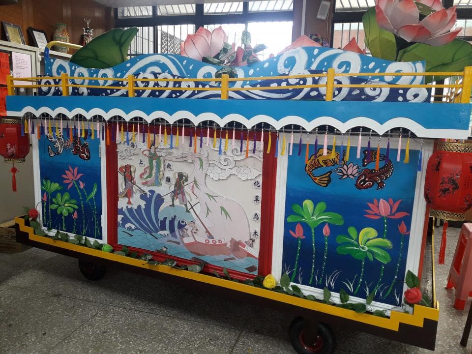 這張照片是一輛彩繪花車,車身兩側都繪有精緻的圖案,包含人物、花草、魚類等等。車頂上的裝飾也十分華麗,呈現出喜慶的氛圍。