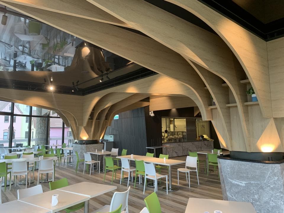 這張「木質拱形屋頂」的照片是一個現代化的餐廳,有許多桌椅,地板是木質的,牆壁是淺色的,天花板有許多拱形結構。