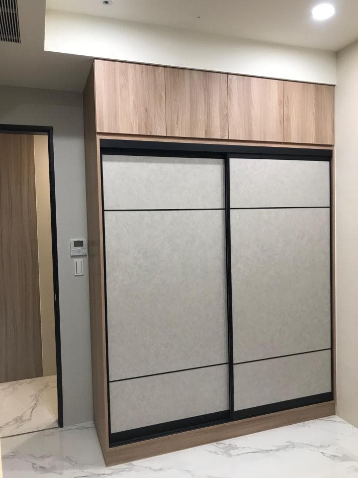 1) 照片顯示一個現代的衣櫃,配備了淺色木紋的門板和滑軌,衣櫃上方的櫃子也是木紋的