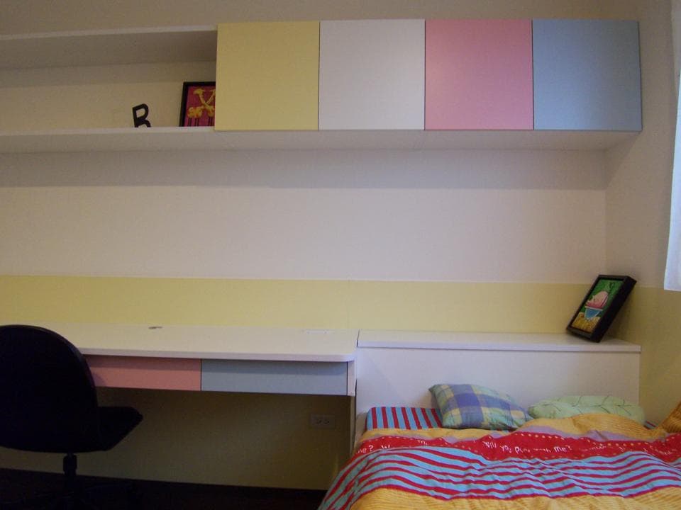 這張照片是一間臥室,房間裡有張床和一張書桌,書桌上方的櫃子很有特色,櫃子分成好幾個顏色。