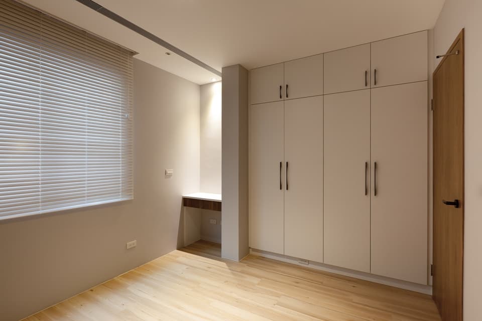這張照片是一間臥室,最顯眼的是一面大型白色衣櫃,衣櫃上有黑色把手,下方有木質地板,看起來十分簡約時尚。