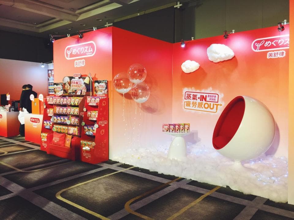 這張「產品宣傳」的照片是,展示了許多產品包裝,旁邊有紅色和白色相間的展臺,以及白色雲朵裝飾。