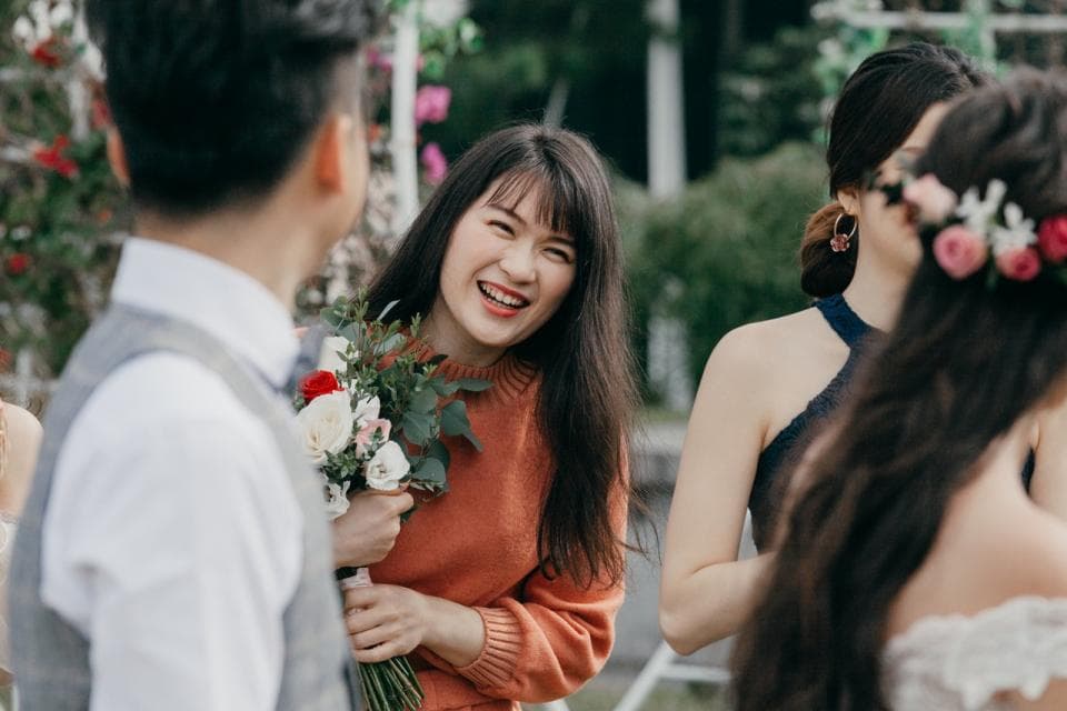 這張「婚禮」的照片是三位女性和一位男性,其中一位女性手持捧花,面帶笑容,並與攝影師有眼神交流,而另一位女性則穿著深色禮服,笑容滿面地看著鏡頭。