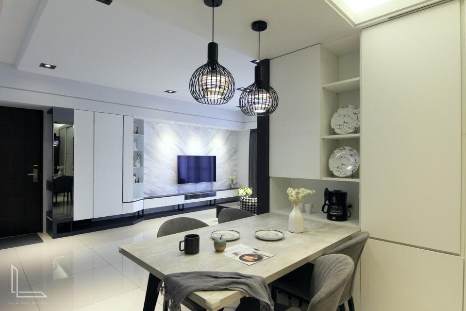 這張「現代化客廳」的照片是一個簡約的空間,牆壁是白色的,地板是淺色的。房間的中心是一個餐桌,上面擺著餐具和一些裝飾品,餐桌旁邊有幾張椅子。房間裡還有電視、壁櫃和幾盞黑色吊燈,整體感覺乾淨、舒適。