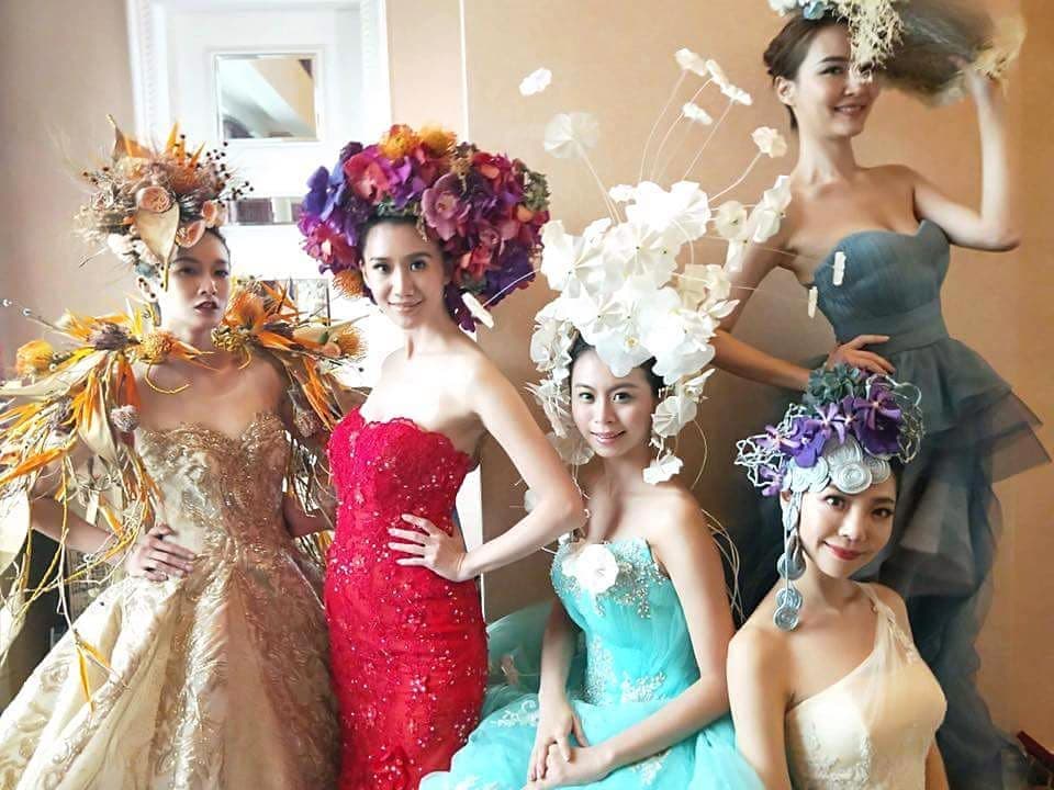 這張「五位女性戴著華麗花飾,穿著禮服」的照片是,她們看起來像是參加婚禮或其他重要場合。她們的笑容和禮服都非常亮眼。