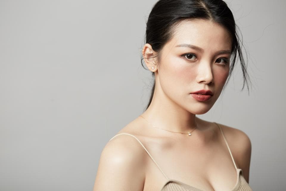 這張照片是一個年輕女性的肖像,她有著烏黑亮麗的頭髮和一雙深邃的眼睛,她身穿一件簡約的吊帶背心,臉上帶著一抹淡淡的微笑,散發出自信和優雅的氣質。