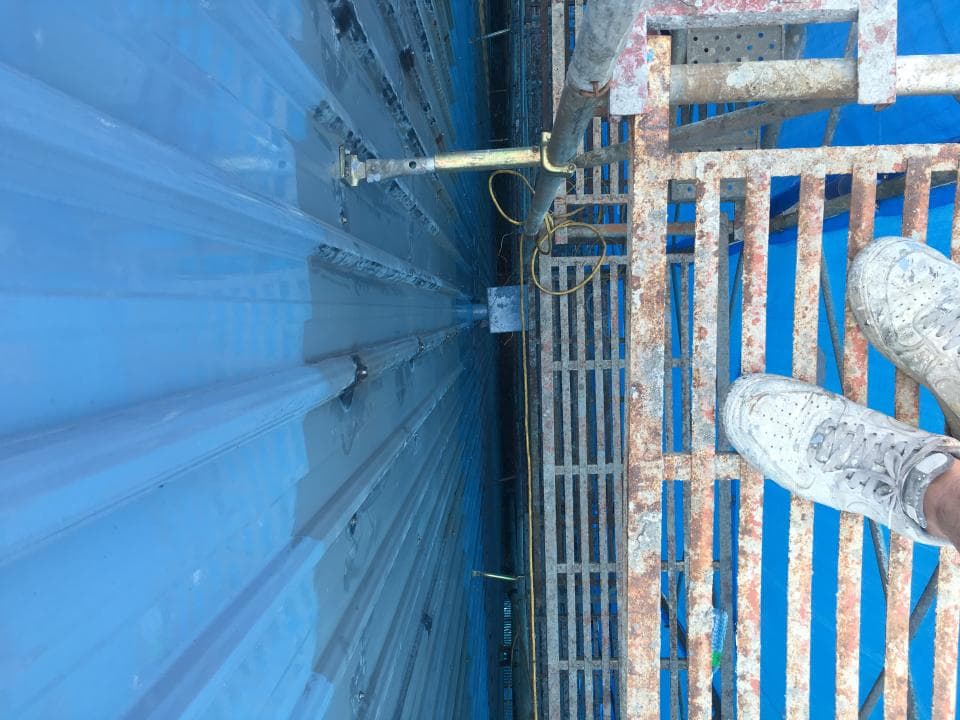 1) 照片顯示一個正在建造中的建築物,建築物外牆是藍色的金屬板,地板是金屬網格狀,有一個人站在地板上,腳穿著白色運動鞋