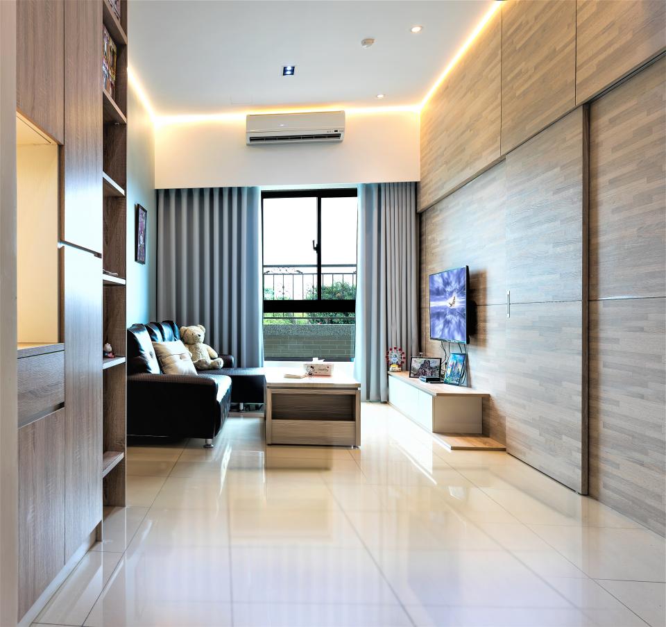 這張「現代風格客廳」的照片是一個明亮的空間,有著木質地板、大窗戶和灰色布藝沙發。牆上裝飾著木質板材,並配備電視。房間裡還有一個咖啡桌和一個大型書櫃。