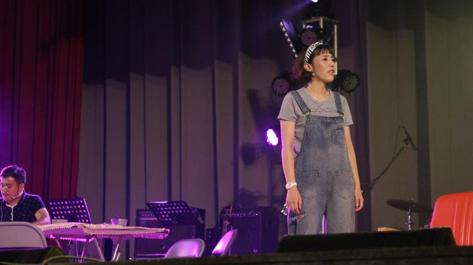 這張照片是一個舞臺表演,照片中一位穿著牛仔吊帶褲的女生正在唱歌,她看起來很投入,表情也很生動。