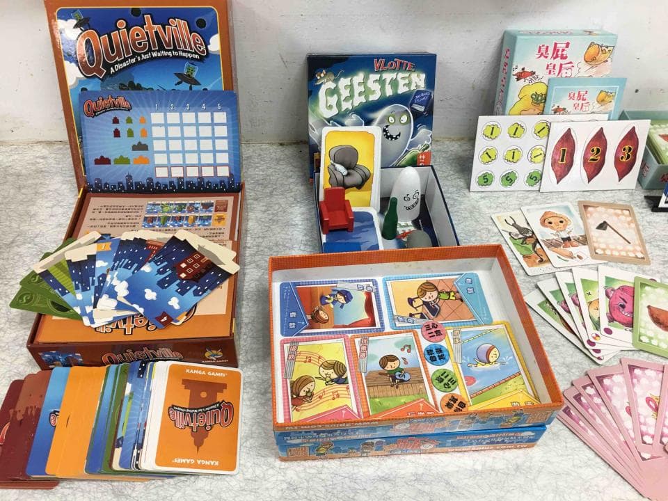 這張照片是一個遊戲桌,上面擺滿了各式各樣的遊戲,其中最顯眼的是一個叫做“Quietville”的遊戲,它的盒子上有著可愛的卡通圖案,並且寫著遊戲名稱和介紹。