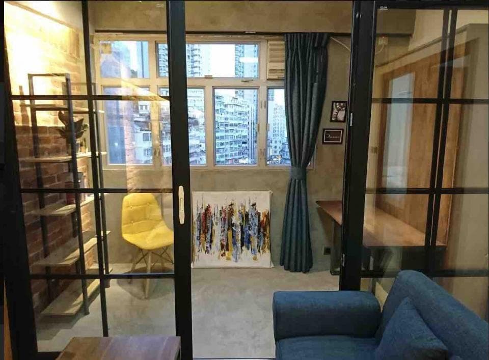 這張室內設計的照片是一個現代化的客廳,有黑色金屬框架的玻璃門,一個黃色的椅子,以及一個藍色的沙發。牆上有一幅抽象畫,房間裡還有窗戶和一個架子。