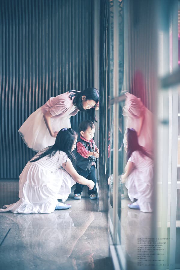 這張照片是一群人在一個現代化的大空間裡玩耍。照片裡,一個女孩穿著粉色裙子,正在和另一個女孩玩捉迷藏。