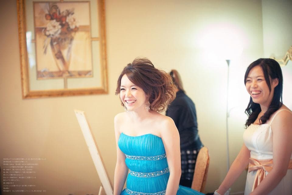 這張照片是一個年輕女子穿著淺藍色的禮服,她微笑著看著相機,她站在另一位穿著白色禮服的女子旁邊,她們看起來非常開心。