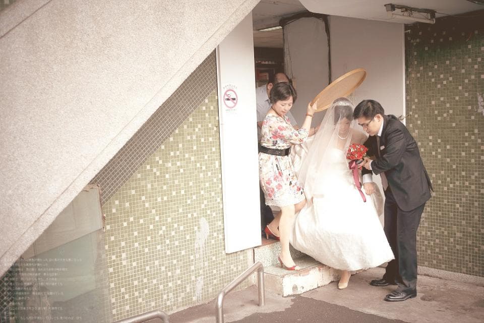 這張照片是一對新人正在舉行婚禮,新娘穿著白色婚紗,新郎則穿著黑色西裝。新郎正扶著新娘走下樓梯,新娘手持一束紅色花束,喜悅洋溢。