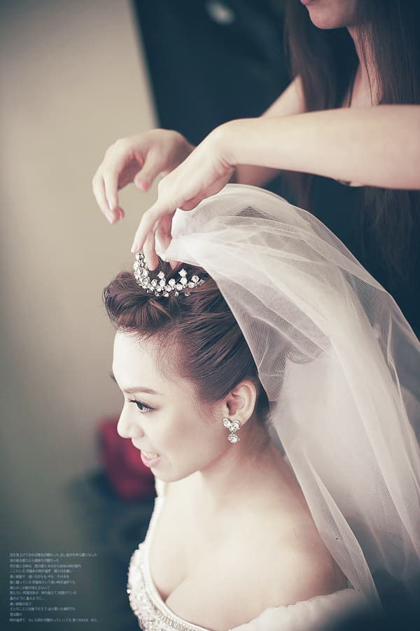 這張照片是一個新娘正在戴著頭紗,她的臉上充滿著喜悅。