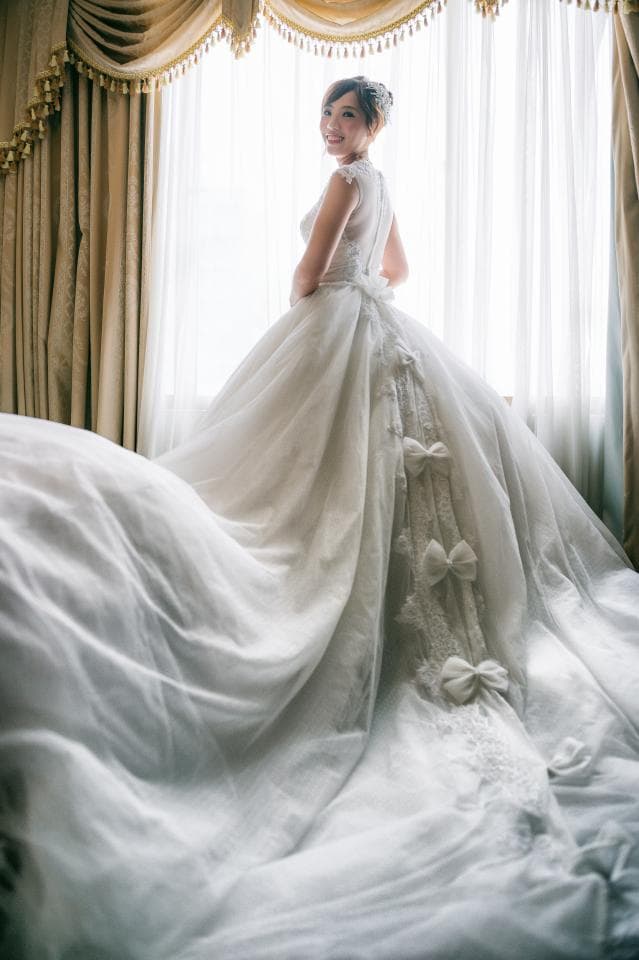 這張照片是一個穿著白色婚紗的女子,站在窗邊,她轉過身,微笑看著鏡頭,她的婚紗非常漂亮,蓬鬆而飄逸。