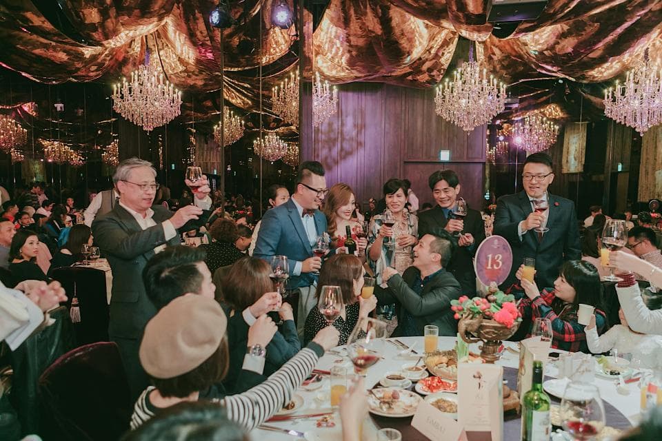 這張照片是婚禮宴會的歡樂場面,賓客們舉杯歡慶,笑容滿面,氣氛熱烈。