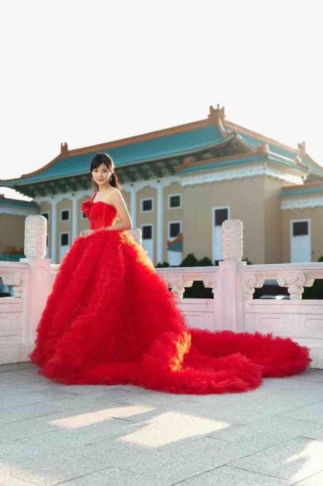 這張照片是一個穿著紅色蓬蓬裙的女孩,她站在一座中國建築物前。她微笑著,看起來很開心。