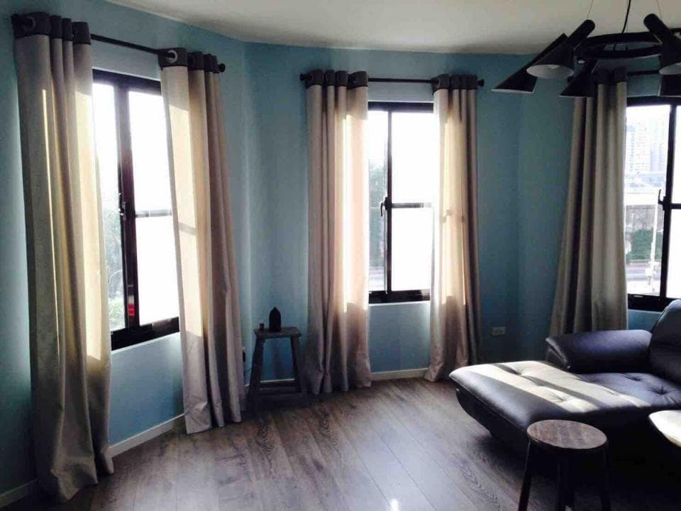 1) 照片中展示了一個藍色牆壁的客廳,有三個窗戶,窗戶上都有米色的窗簾,地板是木地板,房間裡有一張黑色的沙發,在沙發旁邊有一個小桌子