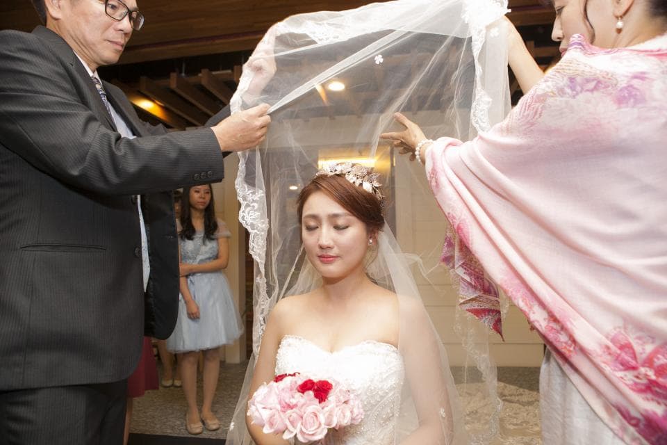 這張「婚禮」的照片是一個穿著婚紗的新娘,她的頭上被蓋著一層白紗,她的父母正在為她舉行蓋頭紗儀式。