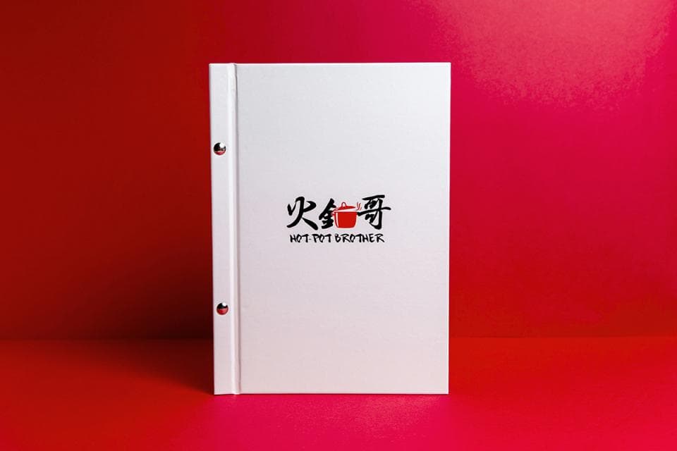 這張「火鍋」的照片是一本白色菜單,上面印著「火鍋」兩個字和一個紅色的鍋子圖案。