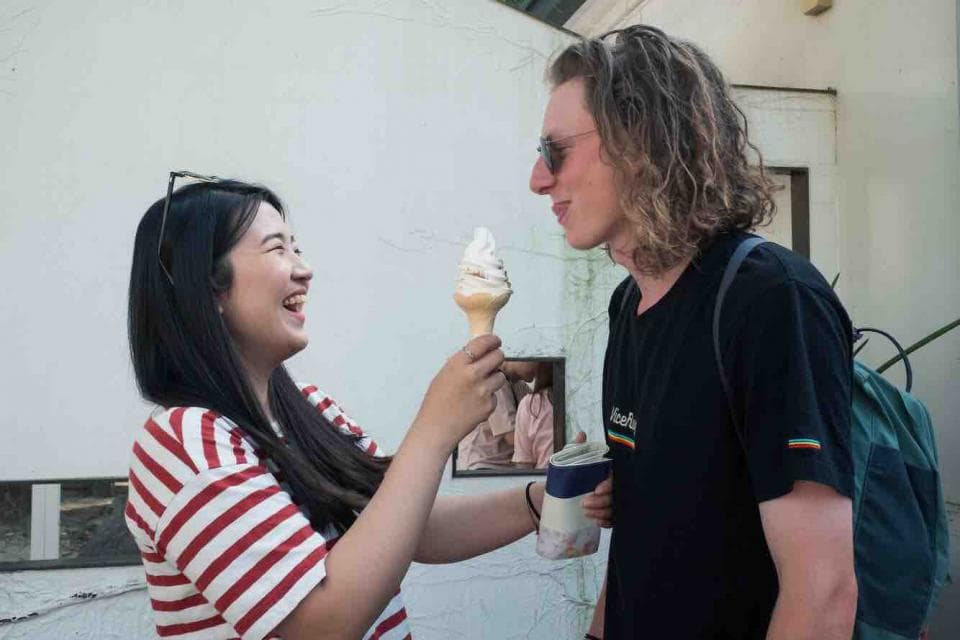 這張「女生拿著冰淇淋,男生看著她的」的照片是兩個年輕人站在一起,女生拿著一個冰淇淋,看起來很開心,男生則看著她。