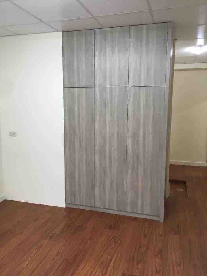 這張照片是一個房間,房間裡有一面灰色的木板牆,木板牆上裝有六個門板,門板上有木紋,牆壁下方是紅棕色的木地板。