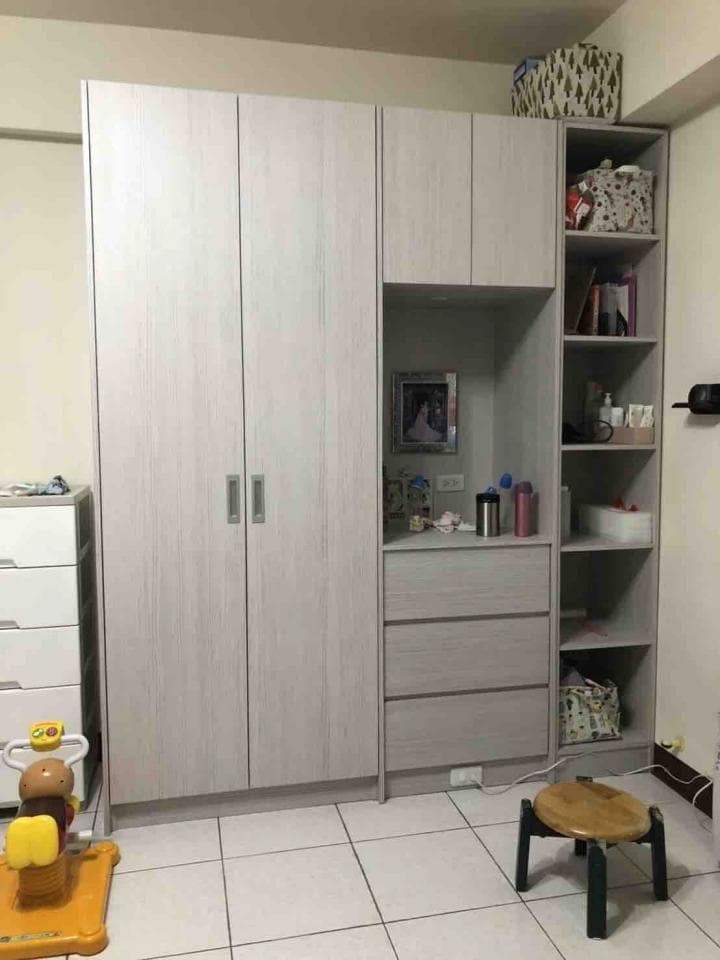 這張照片是一間臥室,房間裡有一個很大的白色衣櫃,中間是開放式層架,旁邊有一個小凳子。