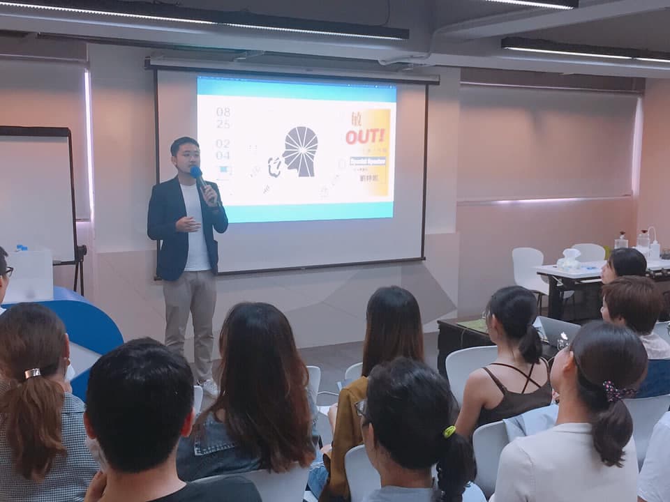 這張照片是一場講座,主講者正在臺上分享內容,臺下坐著許多聽眾專心聆聽。