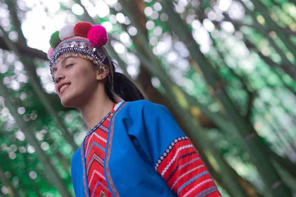 這張照片是一個穿著傳統服飾的年輕女性,她戴著一頂有彩色球的帽子,並且微笑著看著鏡頭。