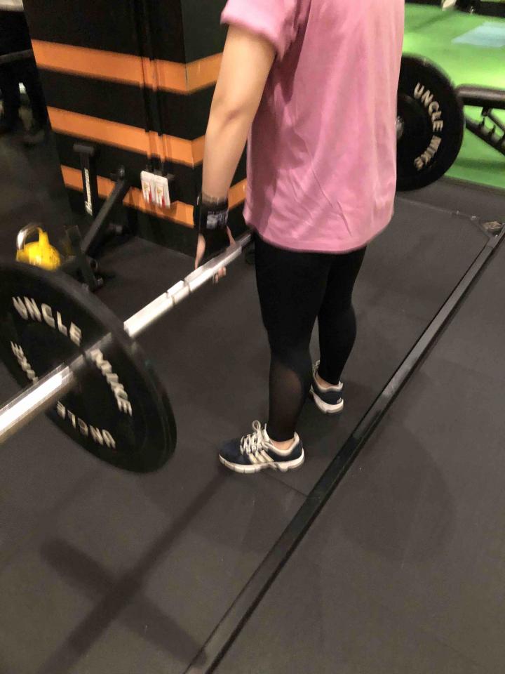 這張照片是一名女子正在健身房舉重。她正在舉起一個槓鈴,她的姿勢很標準,她的肌肉也很發達。