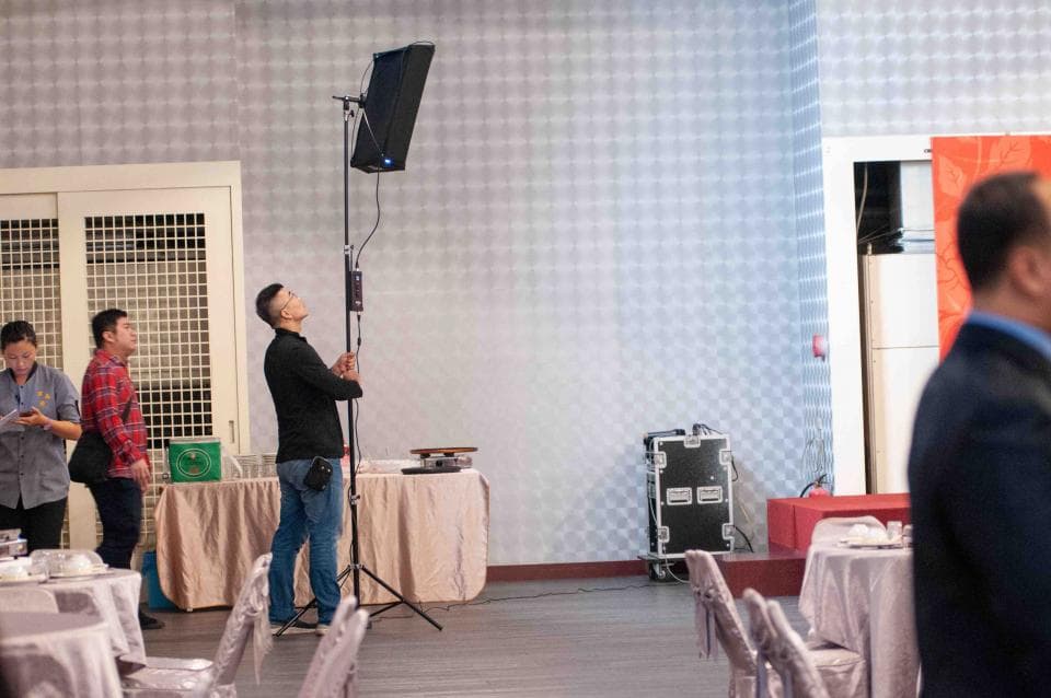 這張「攝影棚」的照片是一個攝影師正在調整燈光,旁邊有一個人在看,還有桌子和椅子。