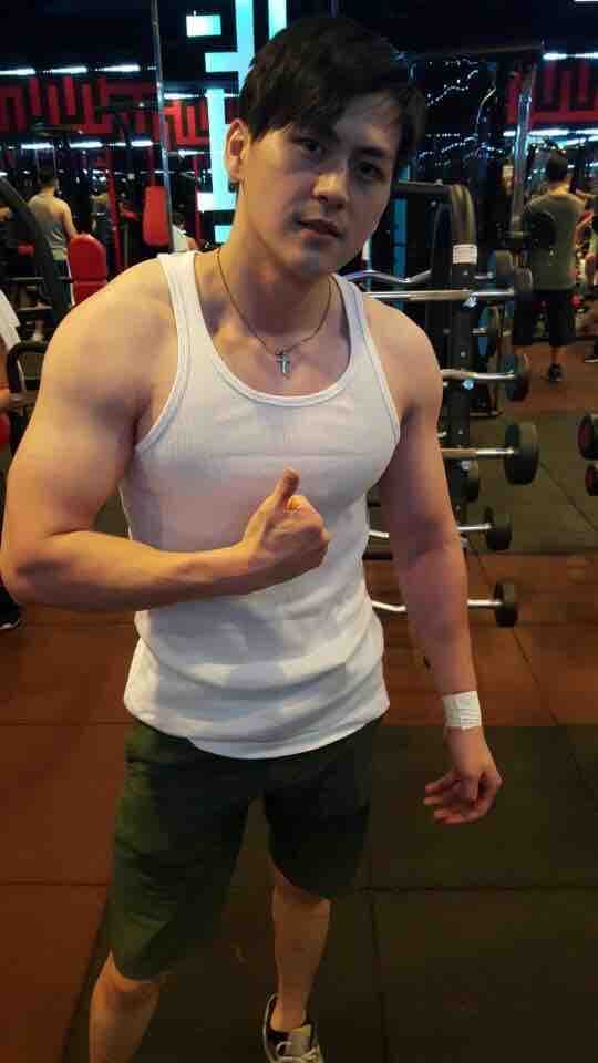 這張「健身房」的照片是一個穿著白色背心和綠色短褲的年輕男子,他正在健身房裡舉重。