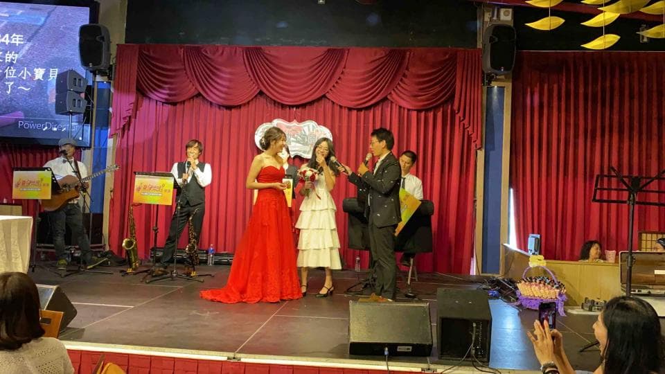 這張照片是一對新人正在臺上舉行婚禮,新娘穿著紅色婚紗,新郎穿著西裝,他們正在交換戒指,並互相深情地望著對方。