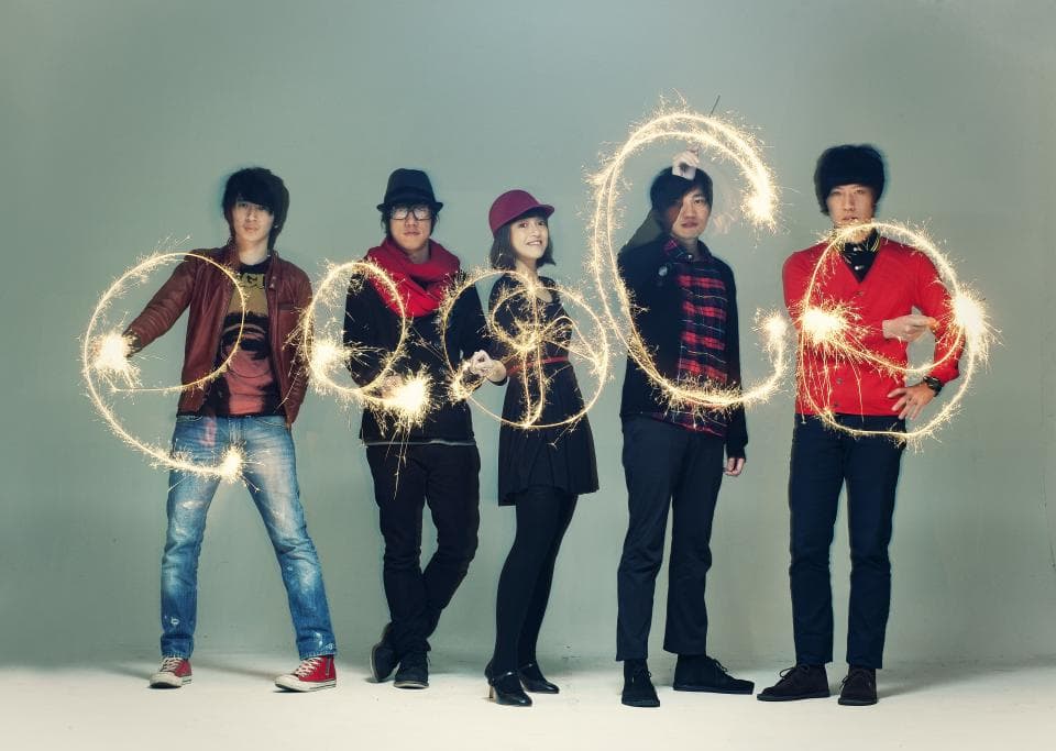 這張「五個年輕人手持煙火」的照片是,他們站在淺灰色背景前,笑容滿面,看起來很開心。