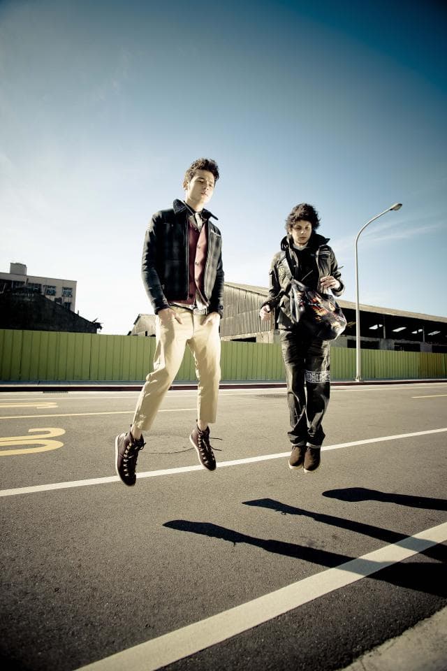 這張照片是兩個年輕人走在路上,其中一個正在跳躍。他們穿著休閒服,看起來很開心。