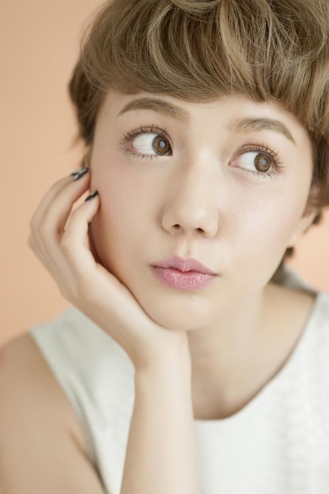 這張「女性肖像」的照片是一個年輕女性,她有著短而微卷的棕色頭髮,穿著白色上衣,用手託著下巴,眼神看起來有點憂鬱。