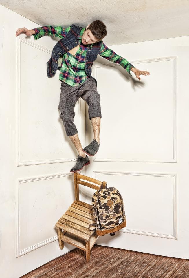 這張「年輕男子站在椅子上,穿著格子襯衫和牛仔褲,手裡拿著揹包」的照片是。