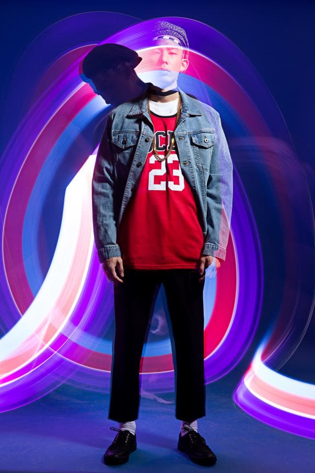 這張「男子站在光圈中的」的照片是一個年輕男子,他穿著牛仔外套、紅色 T 恤和黑色褲子,站在藍紫色和粉色的光圈中。