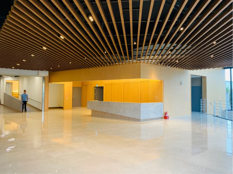 這張「現代建築大廳」的照片是一個寬敞的空間,擁有木質格柵天花板、明亮的牆壁,以及一個簡潔的接待臺。地板是光滑的拋光地板,整個空間明亮而整潔。