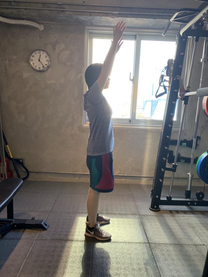 這張照片是一個人在健身房做伸展運動。他舉起雙手,身體伸展得很直,看起來很放鬆。