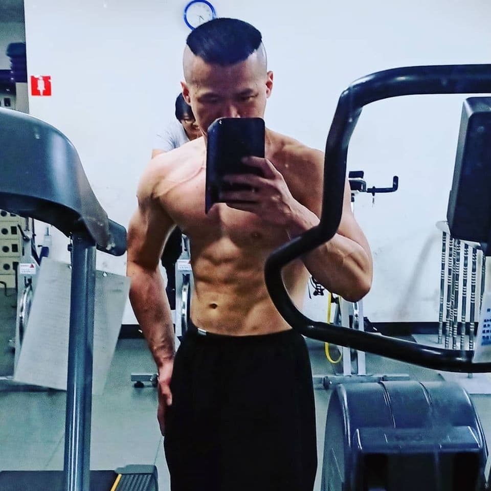 這張「健身房自拍」的照片是一個年輕男子在健身房自拍,他穿著運動褲,露出了健美的肌肉,並拿著手機自拍。