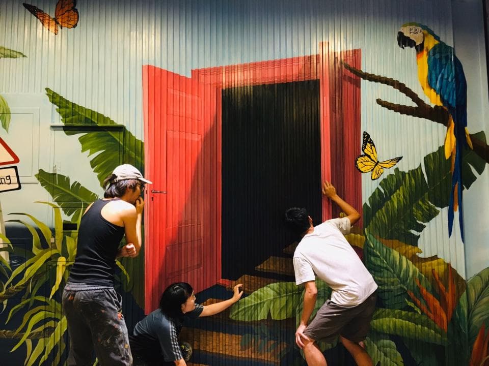 這張「街頭藝術」的照片是一個紅色的門,旁邊是一隻鸚鵡,它站在綠色的樹枝上,看起來很逼真。